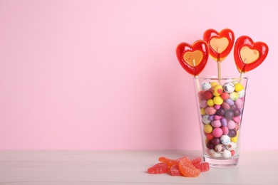 Photo of Delicious heart shaped lollipops, dragees and jelly candies on table against pink background. Space for text
