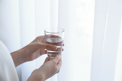 Photo of Woman holding glass of water near window at home, closeup
