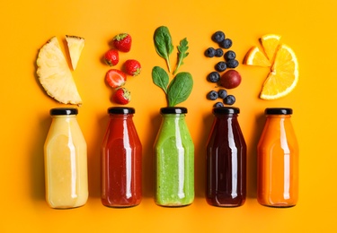 Flat lay composition with bottles of delicious juices and fresh ingredients on orange background