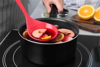 Photo of Woman cooking delicious mulled wine at stove, closeup