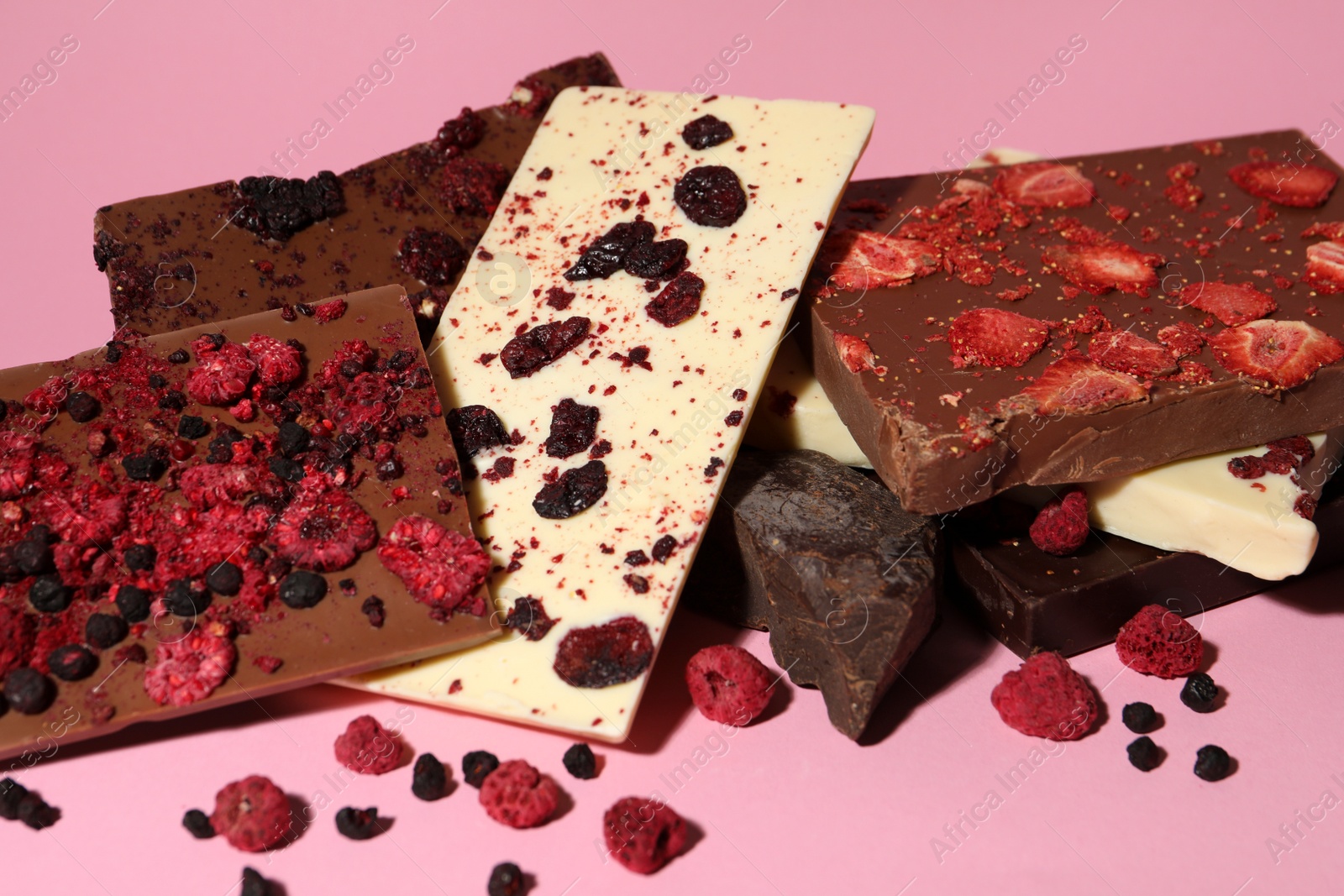 Photo of Different chocolate bars with freeze dried fruits on pink background