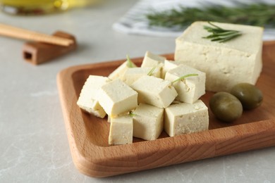 Photo of Pieces of delicious tofu with rosemary and olives on grey table, closeup. Soybean curd