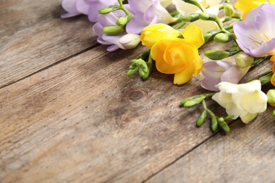 Photo of Beautiful fresh freesia flowers on wooden background, closeup. Space for text