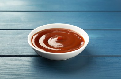 Photo of Tasty barbeque sauce in bowl on blue wooden table