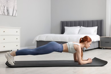 Photo of Young woman in sportswear doing exercises on fitness mat in bedroom