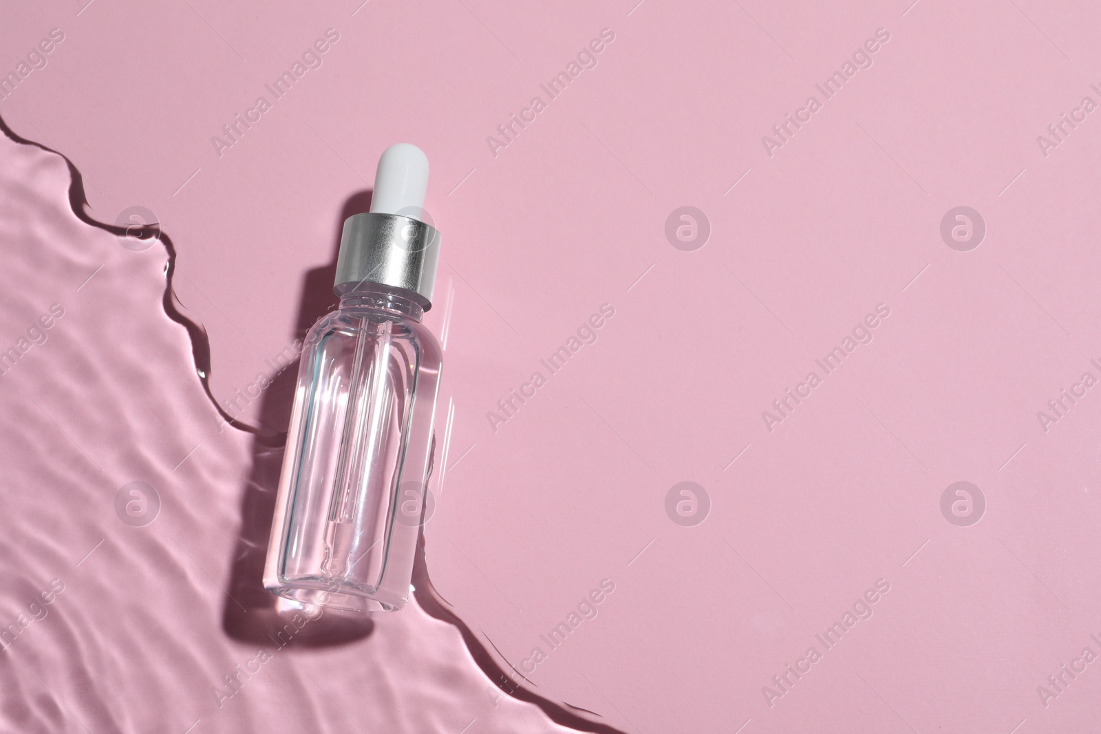 Photo of Bottle of cosmetic oil in water on pink background, top view. Space for text