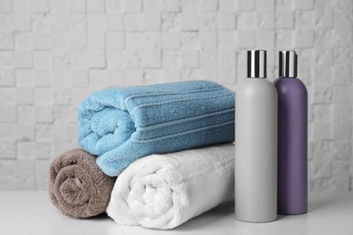 Photo of Rolled towels and shampoo on table against white wall