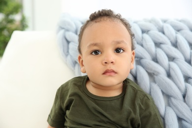 Cute African-American baby in stylish clothes on couch