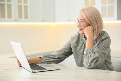 Photo of Beautiful mature woman working with laptop in kitchen