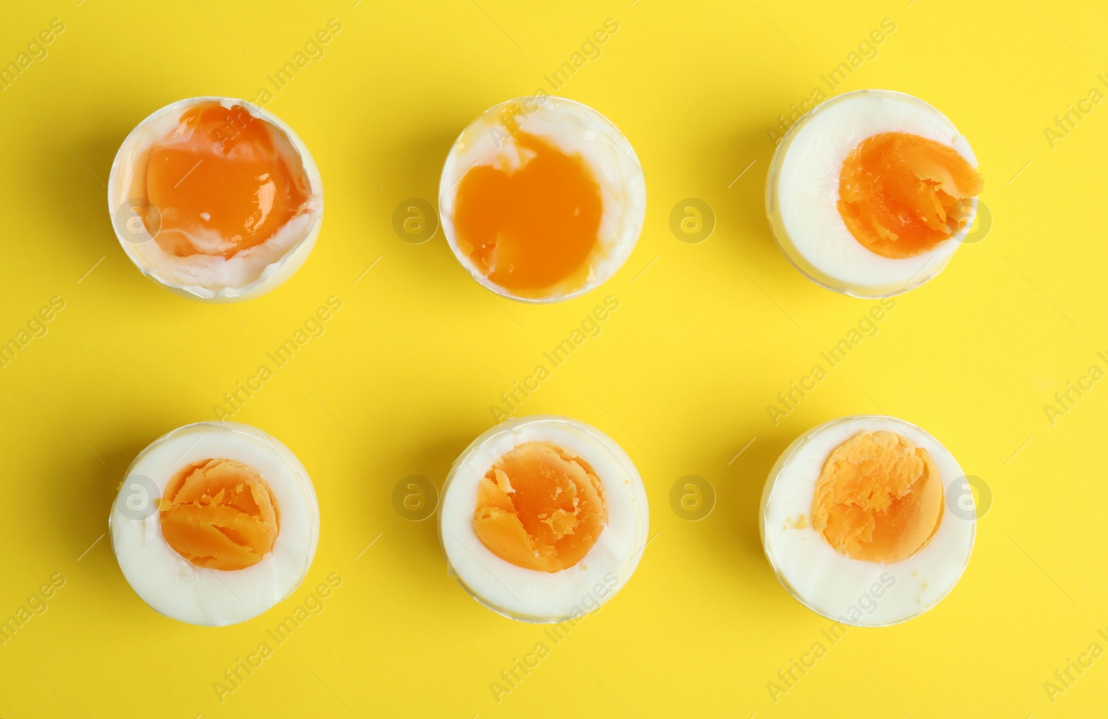 Photo of Different readiness stages of boiled chicken eggs on yellow background, flat lay