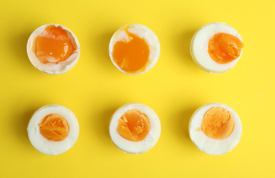 Different readiness stages of boiled chicken eggs on yellow background, flat lay