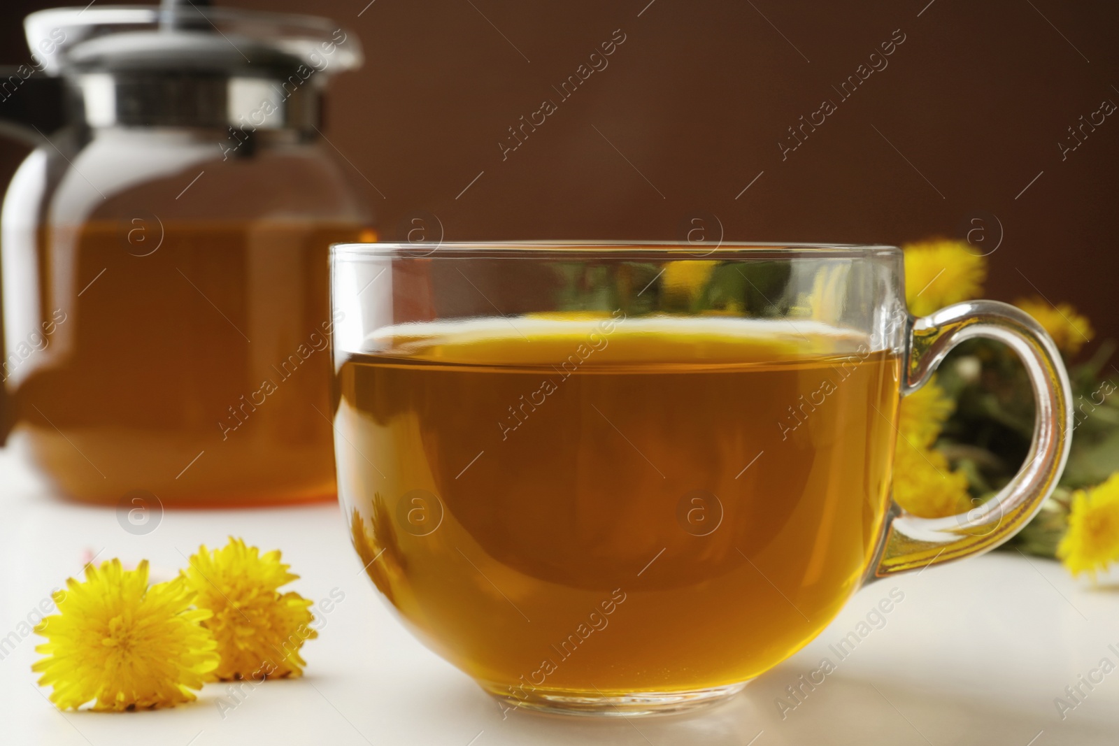 Photo of Delicious fresh tea and beautiful dandelion flowers on white table , closeup