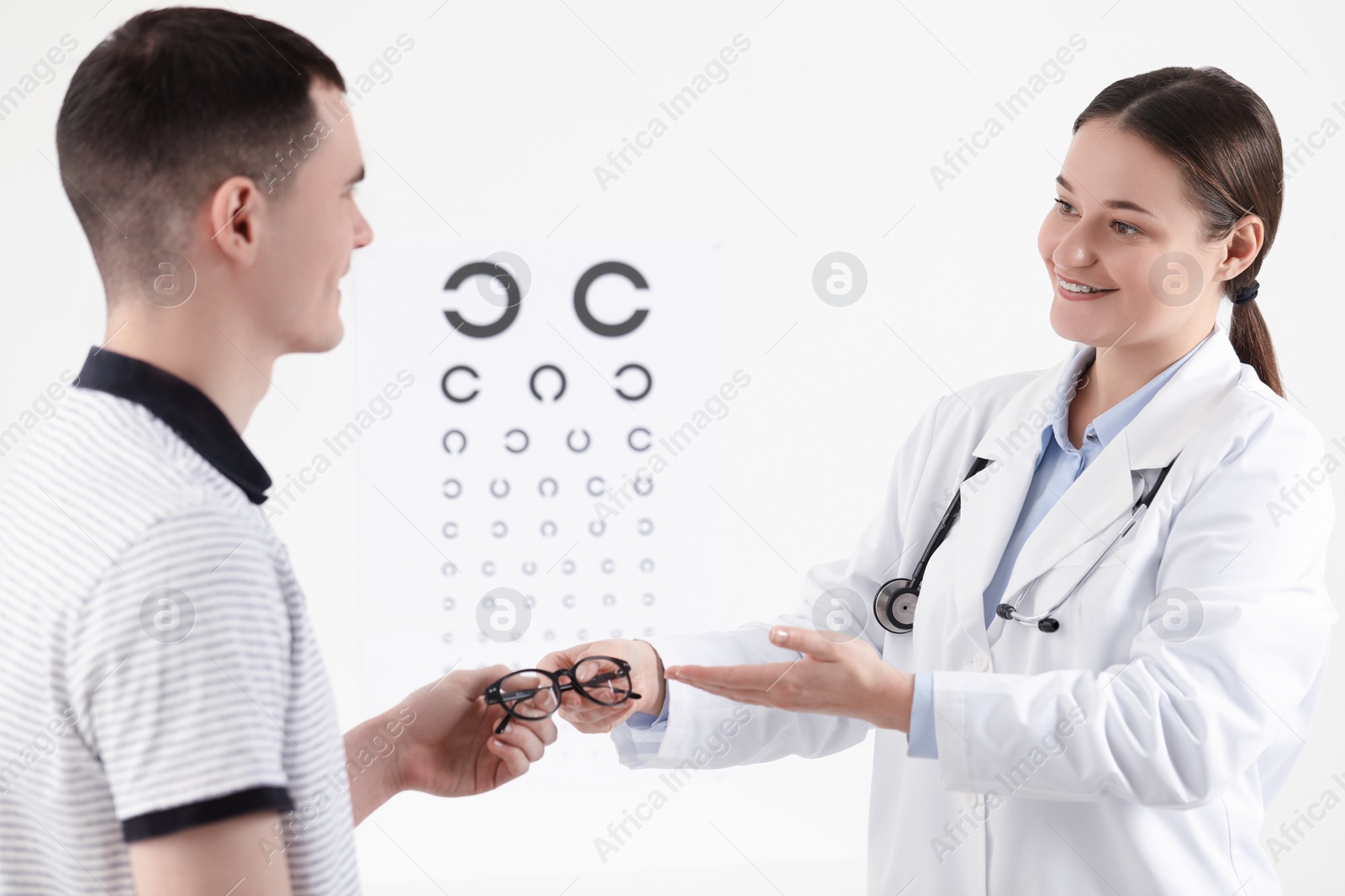 Photo of Vision testing. Ophthalmologist giving glasses to young man indoors