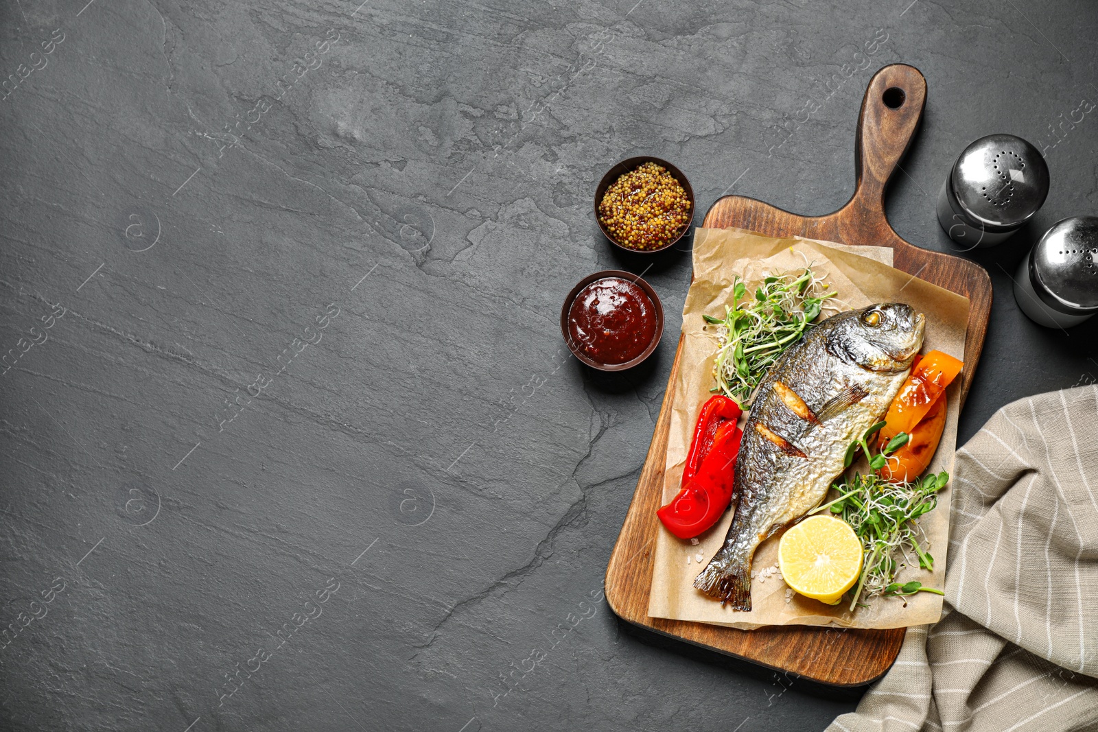 Photo of Delicious roasted fish and vegetables on dark grey table, flat lay. Space for text