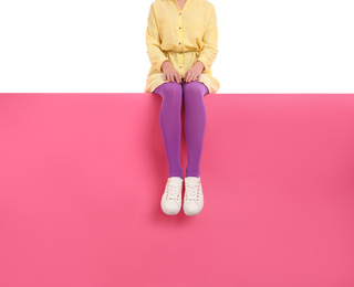Woman wearing bright tights and stylish shoes sitting on color background, closeup