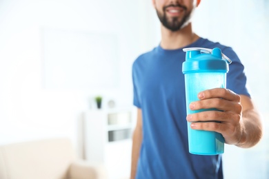 Young man with bottle of protein shake at home, closeup. Space for text