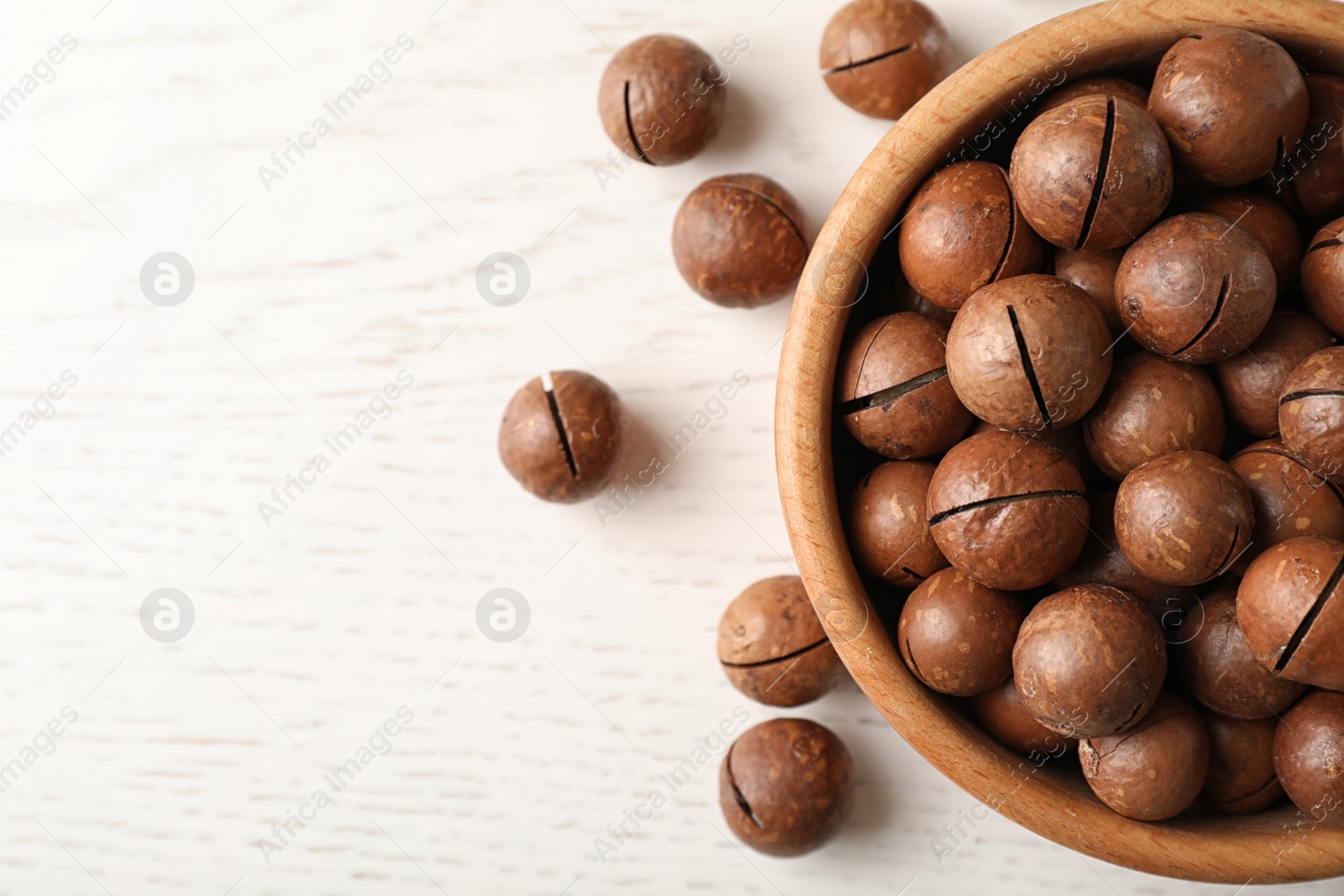 Photo of Bowl with organic Macadamia nuts on wooden table, top view. Space for text