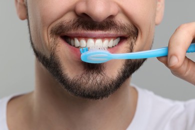 Photo of Man brushing his teeth with plastic toothbrush on light grey background, closeup