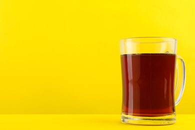 Photo of Delicious homemade kvass in glass mug on yellow background. Space for text