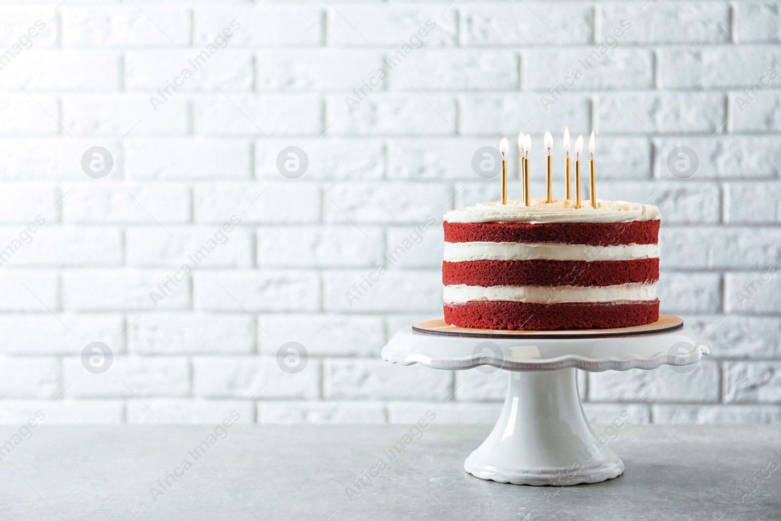 Photo of Delicious homemade red velvet cake with candles on table against brick wall. Space for text