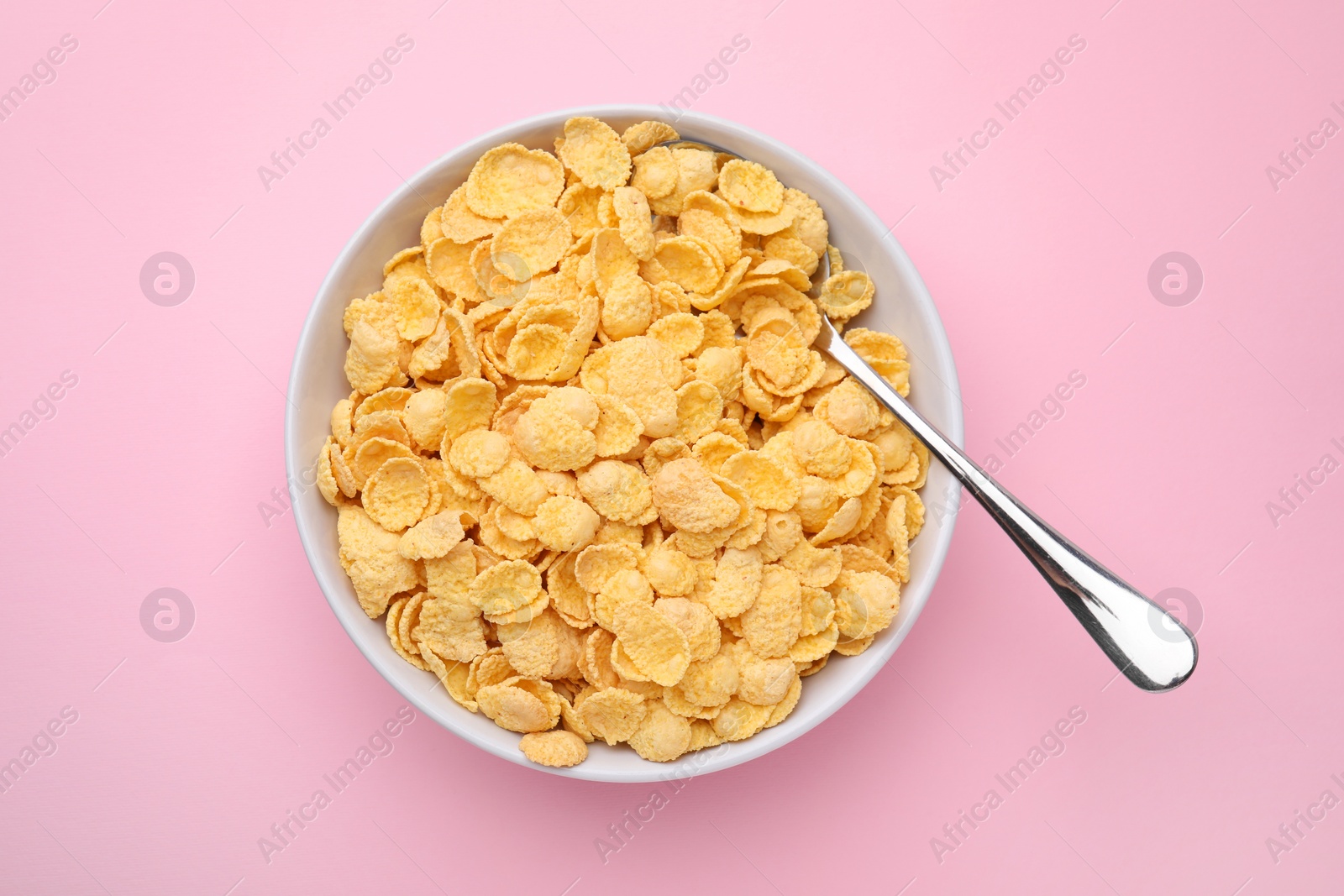 Photo of Breakfast cereal. Tasty corn flakes in bowl and spoon on pink table, top view