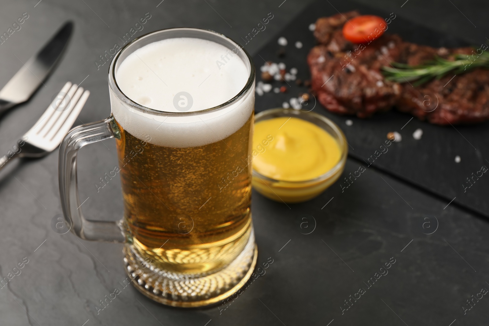 Photo of Mug with beer, delicious fried steak and sauce on black table. Space for text