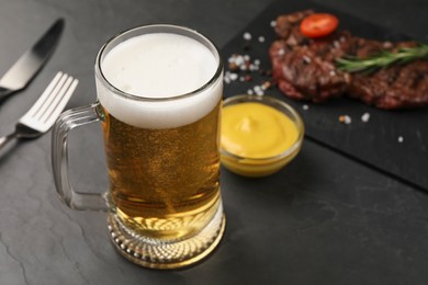 Mug with beer, delicious fried steak and sauce on black table. Space for text
