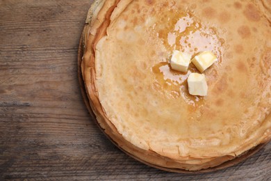 Photo of Stack of delicious crepes with melting butter on wooden table, top view