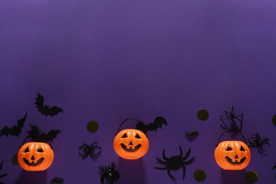 Photo of Flat lay composition with plastic pumpkin baskets, paper bats and spiders on purple background, space for text. Halloween decor