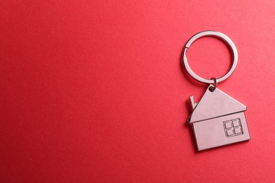 Photo of Metallic keychain in shape of house on red background, top view. Space for text