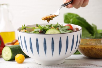 Photo of Woman pouring tasty vinegar based sauce (Vinaigrette) from spoon into bowl with salad at wooden rustic table, closeup