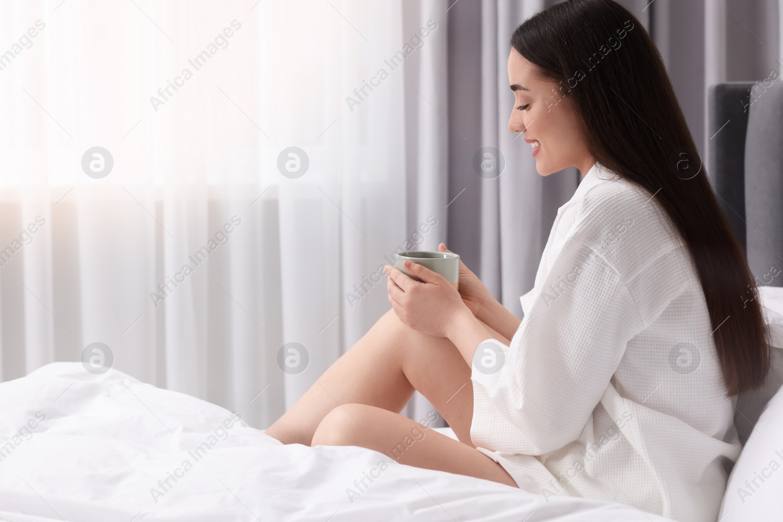 Photo of Happy woman with cup of drink on bed at home, space for text. Lazy morning