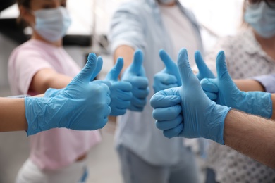 Photo of Group of people in blue medical gloves showing thumbs up on blurred background, closeup