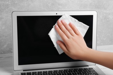 Woman wiping laptop with paper towel at white wooden table, closeup