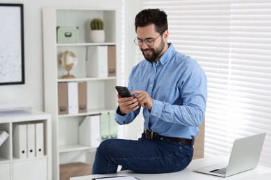 Photo of Happy young man using smartphone in office