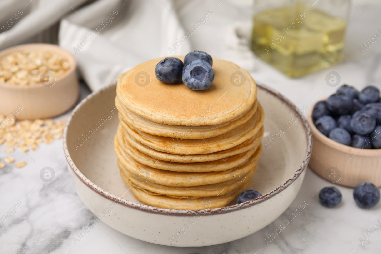 Photo of Tasty oatmeal pancakes with blueberries on white marble table, closeup