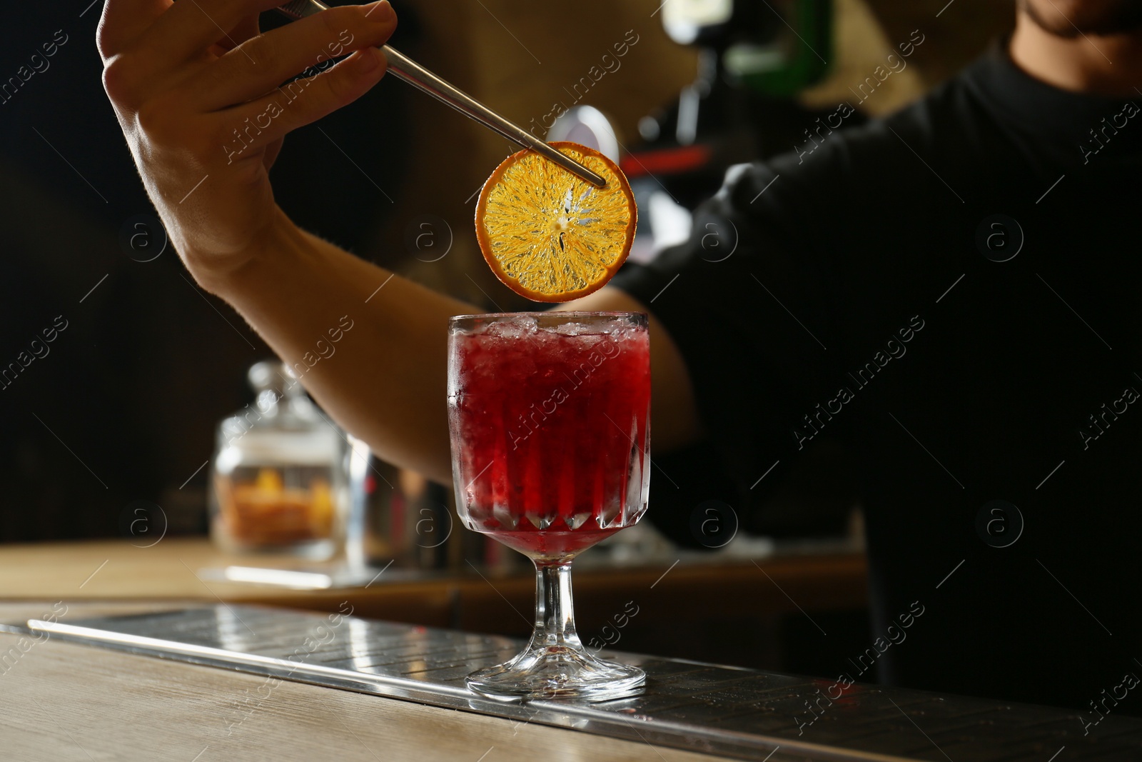 Photo of Bartender decorating glass of fresh alcoholic cocktail at bar counter, closeup