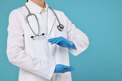 Doctor with stethoscope holding something on light blue background, closeup. Space for text