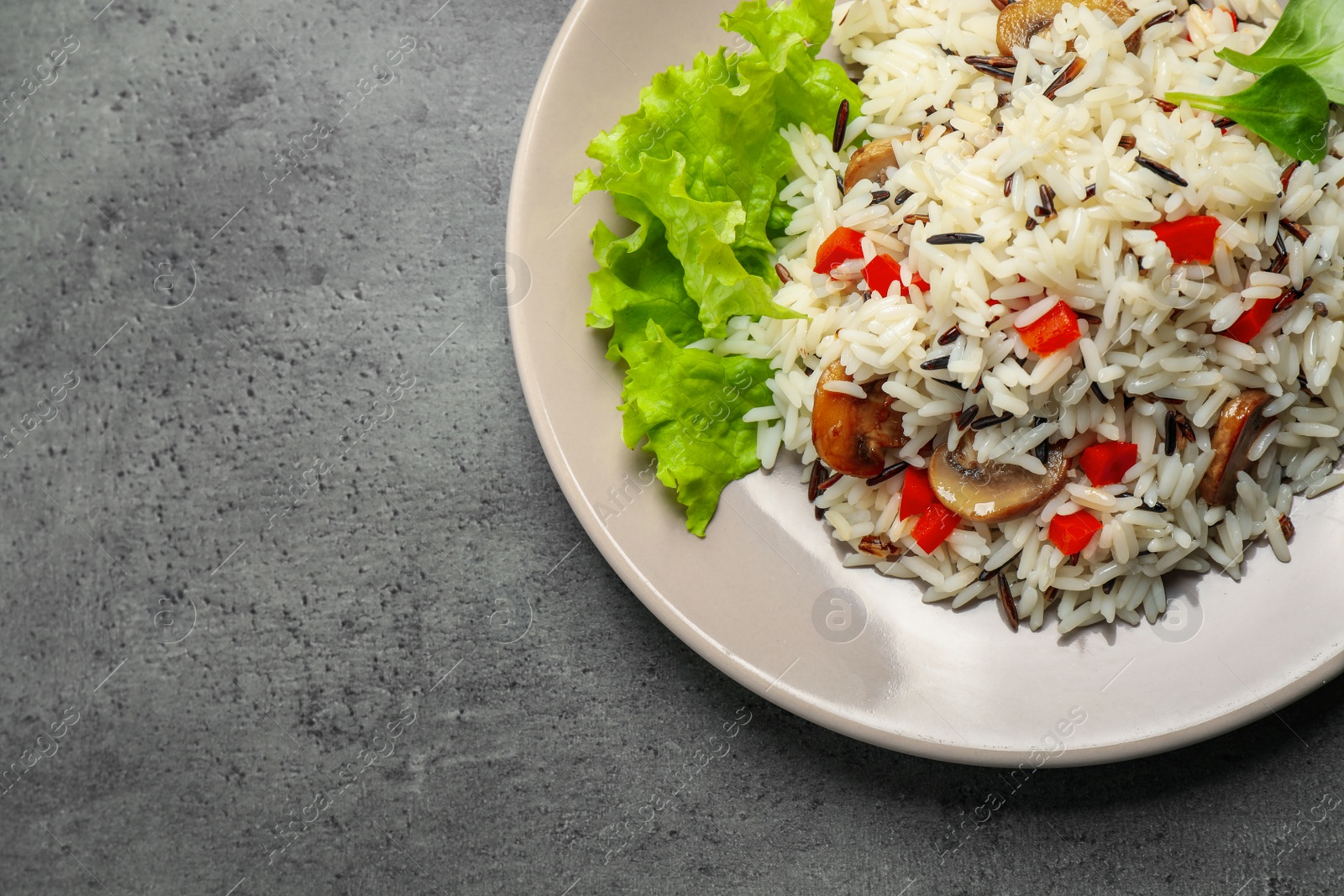 Photo of Delicious rice pilaf with mushrooms on grey table, top view. Space for text