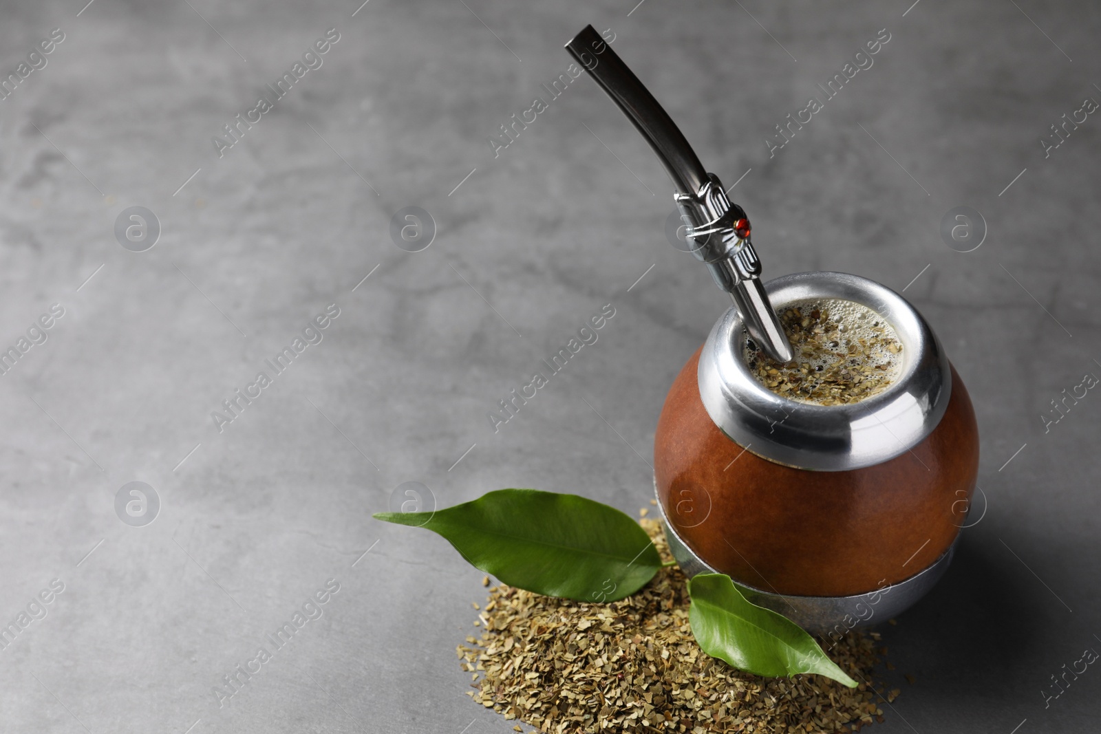 Photo of Calabash with mate tea and bombilla on light grey table. Space for text