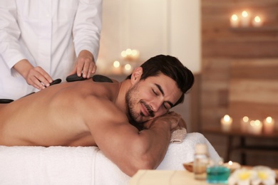 Photo of Handsome young man receiving hot stone massage in spa salon, space for text