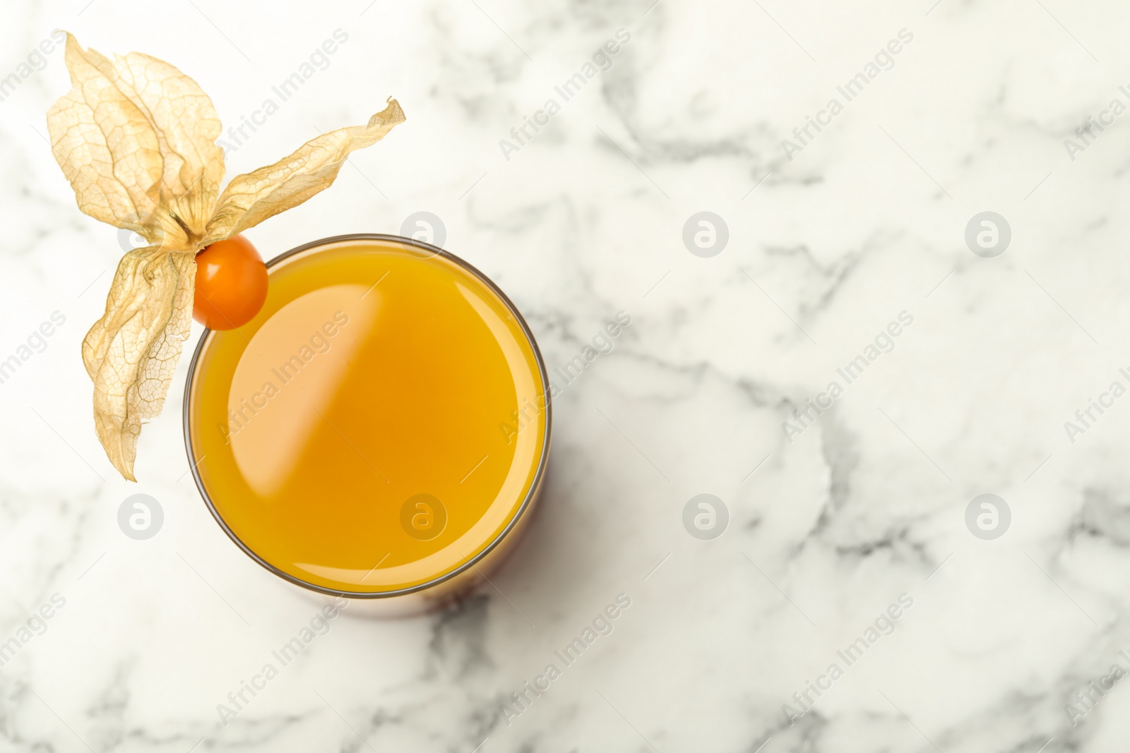 Photo of Refreshing cocktail decorated with physalis fruit on white marble table, top view. Space for text