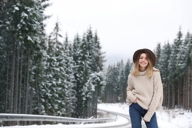 Photo of Young woman near snowy forest, space for text. Winter vacation