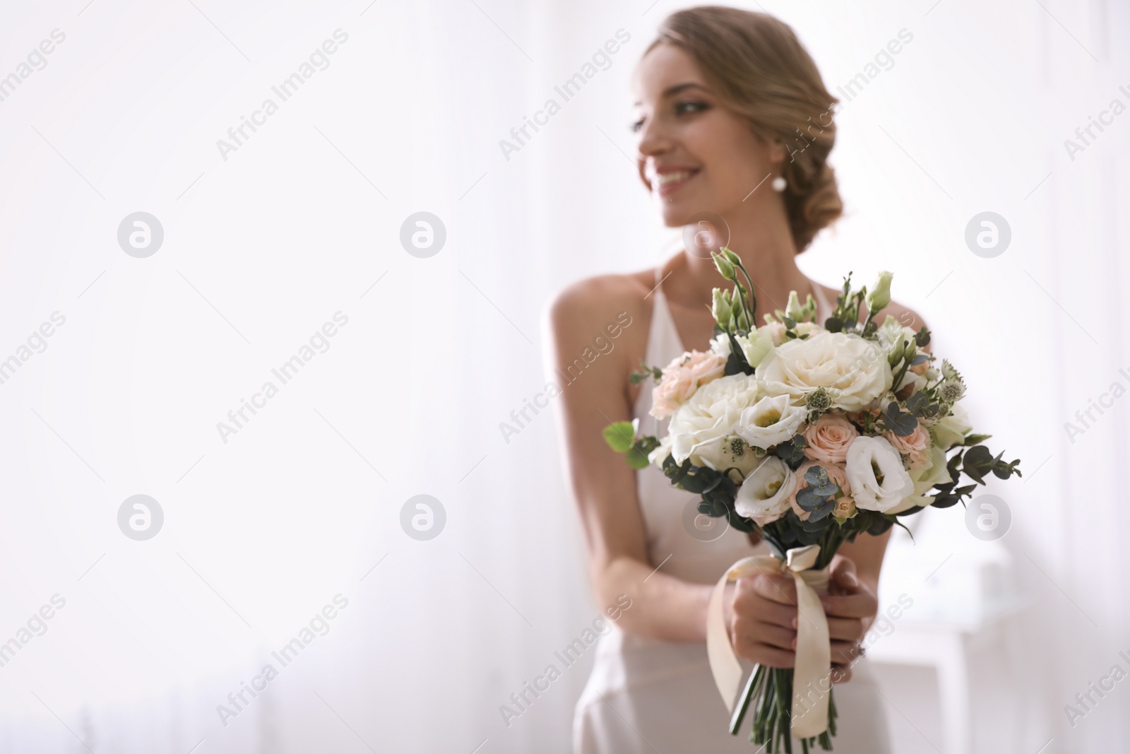 Photo of Young bride with beautiful wedding bouquet in room, focus on flowers. Space for text