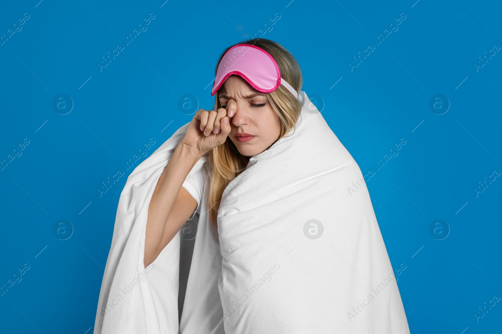 Photo of Young woman in sleeping mask wrapped with soft blanket on blue background