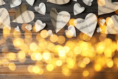 Image of Christmas and New Year music. Hearts cut out from music sheets on wooden background, bokeh effect