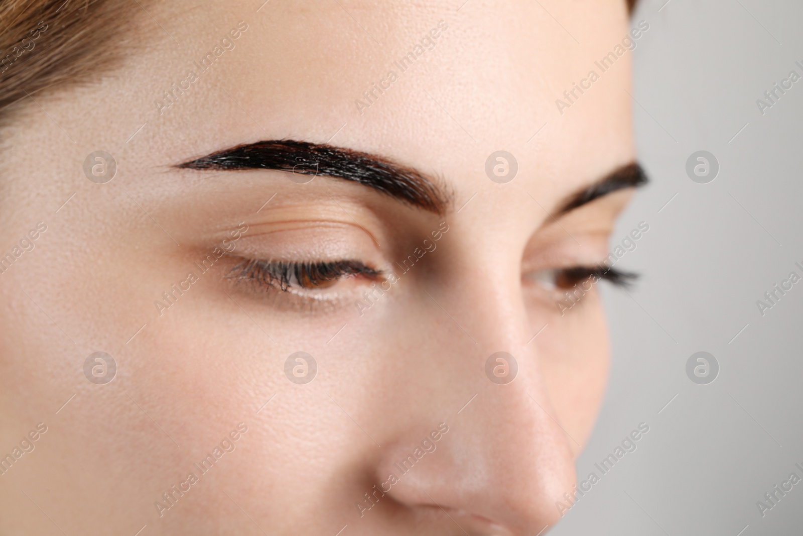 Photo of Woman during eyebrow tinting procedure on grey background, closeup