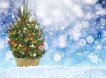 Snow and blurred view of beautiful decorated Christmas tree. Bokeh effect