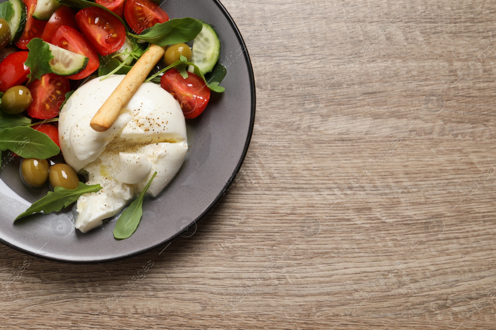 Photo of Delicious burrata salad on wooden table, top view. Space for text