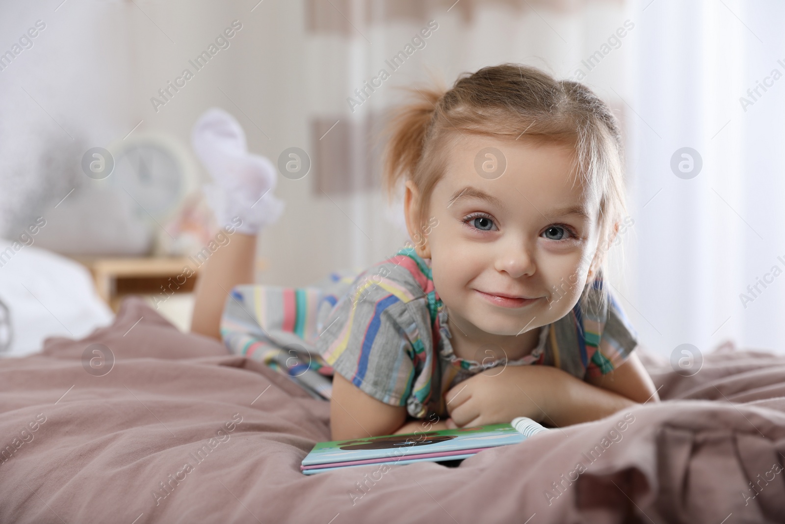 Photo of Cute little girl with book on bed at home